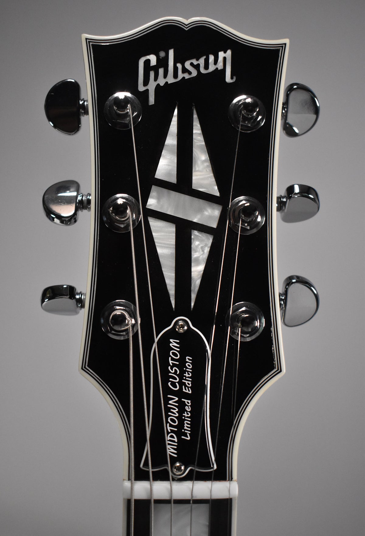 Close-up of the guitar's black headstock with white binding, featuring mother-of-pearl inlays and six chrome tuners.