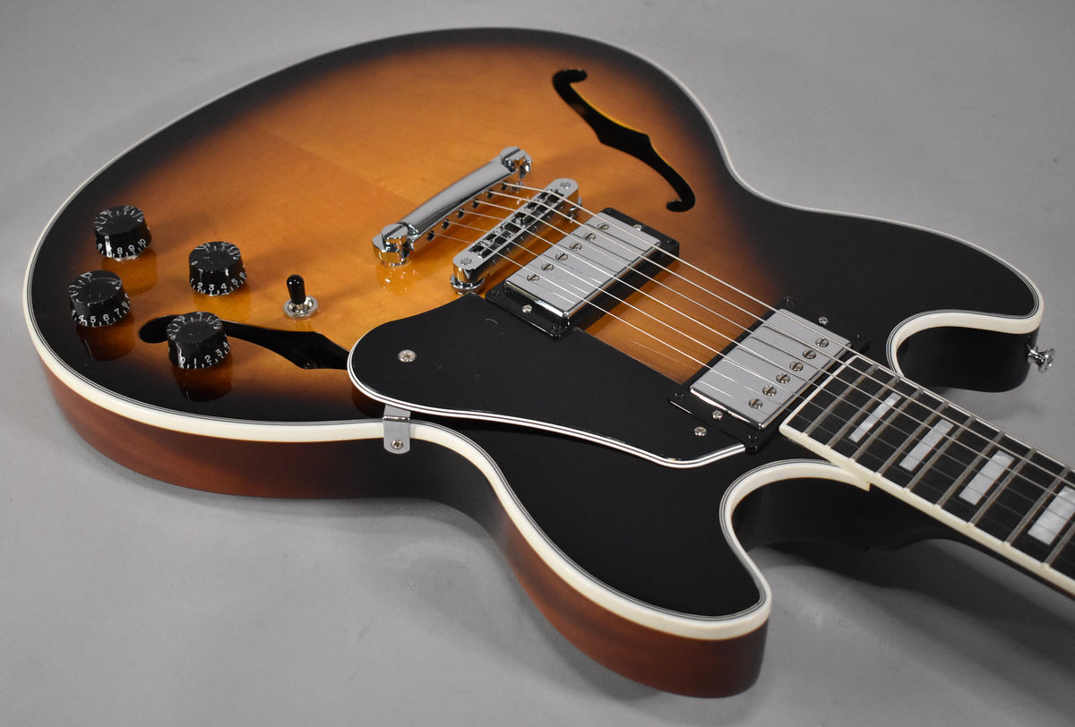 The semi-hollow guitar, angled right, shows its sunburst body, black pickguard, chrome hardware, and four black control knobs.