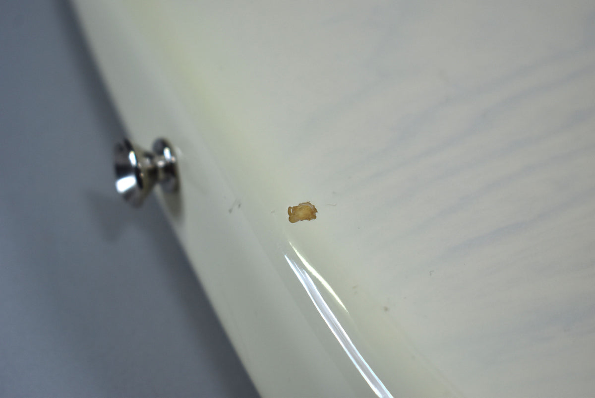 Close-up of the guitar's white body, showing a chrome strap button and a small, irregular chip in the finish revealing a brown layer beneath.