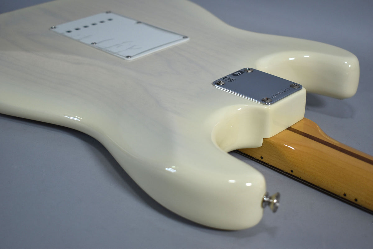 The back of a glossy off-white Stratocaster body, showing the tremolo cavity cover, neck plate, and a light maple neck.