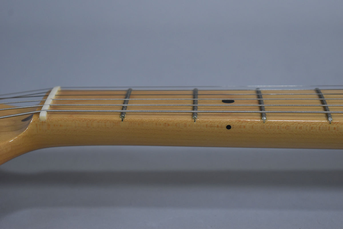 Close-up of the light maple neck and fretboard, showing the nut, frets, strings, and two black dot inlays.