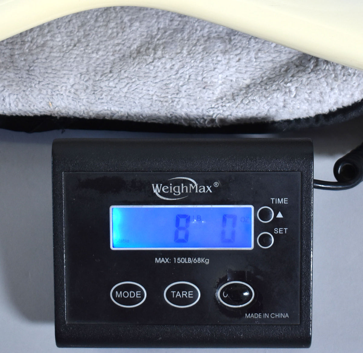 A black digital scale displays "8 LB. 0 OZ." with a light-colored guitar body resting on a gray, plush surface above it.