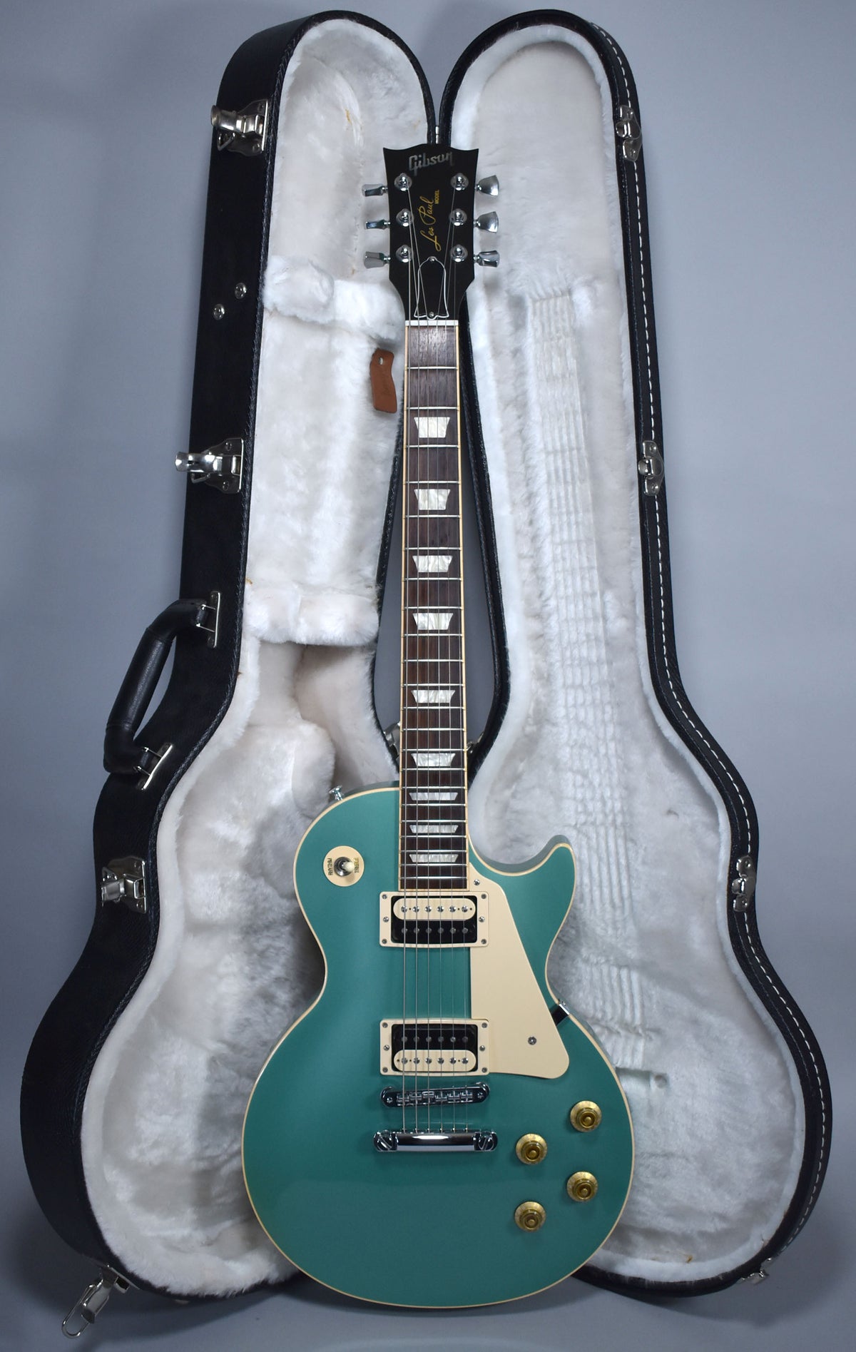 Full-length view of a teal Les Paul with cream binding, pickguard, and pickup rings, resting in an open black hard case.