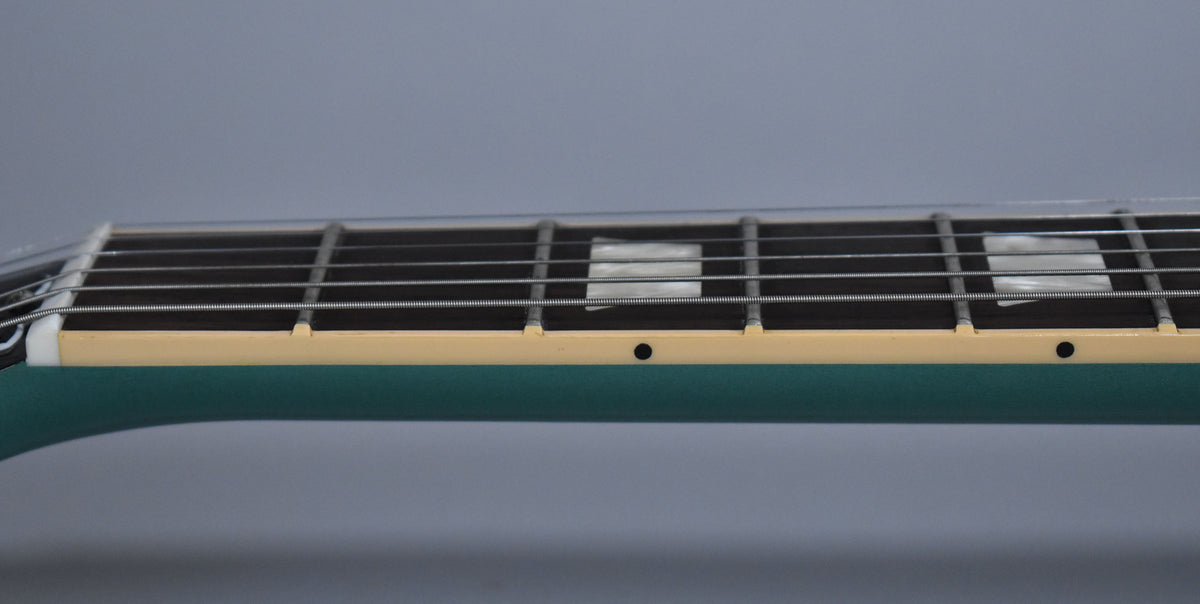 Close-up of the Inverness Green guitar's dark fretboard with trapezoid inlays, cream binding, and side dots, viewed from the bass side.