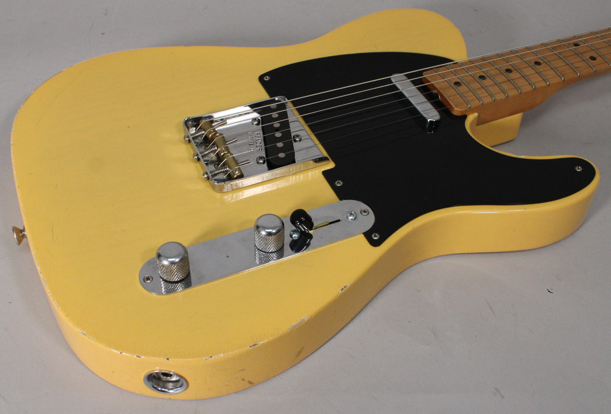 Blonde Telecaster body, angled from the lower bout, showing the black pickguard, chrome bridge, control plate with two knurled knobs, and a 3-way switch.