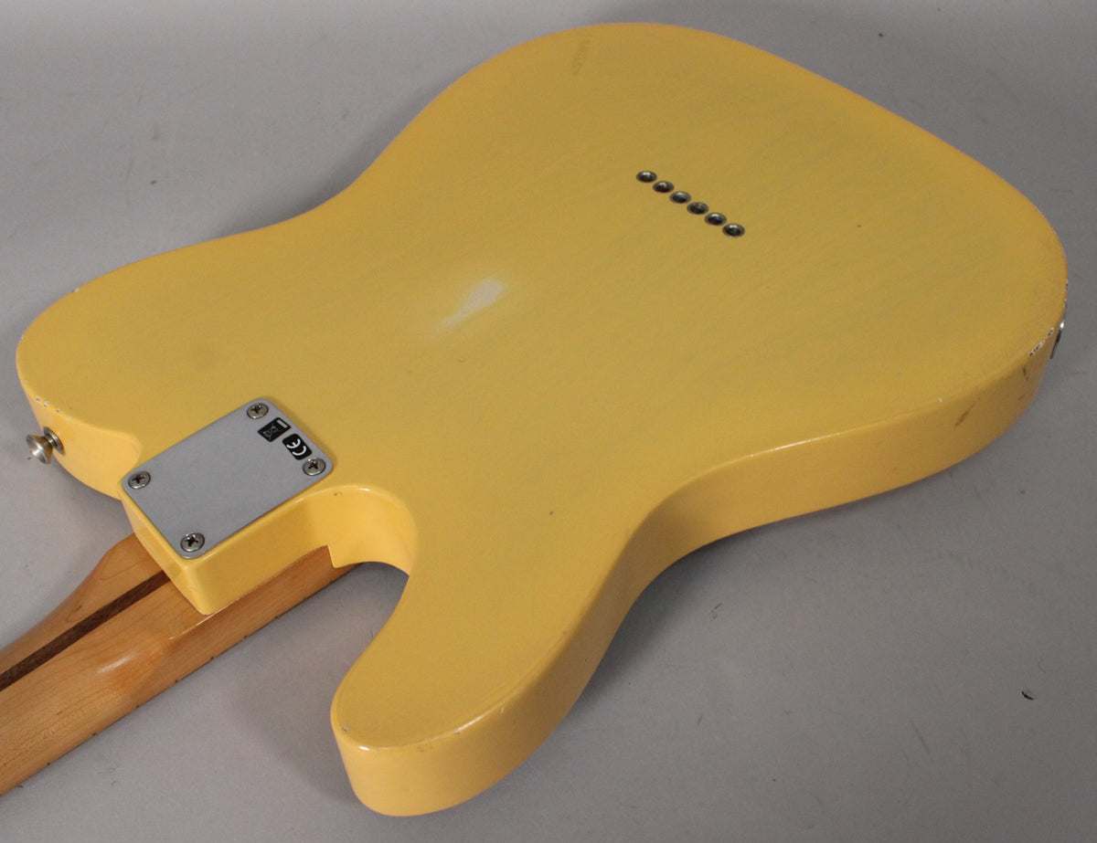 The back of a blonde Telecaster body with a worn finish, showing the neck plate, string-through ferrules, and a few chips on the edges.