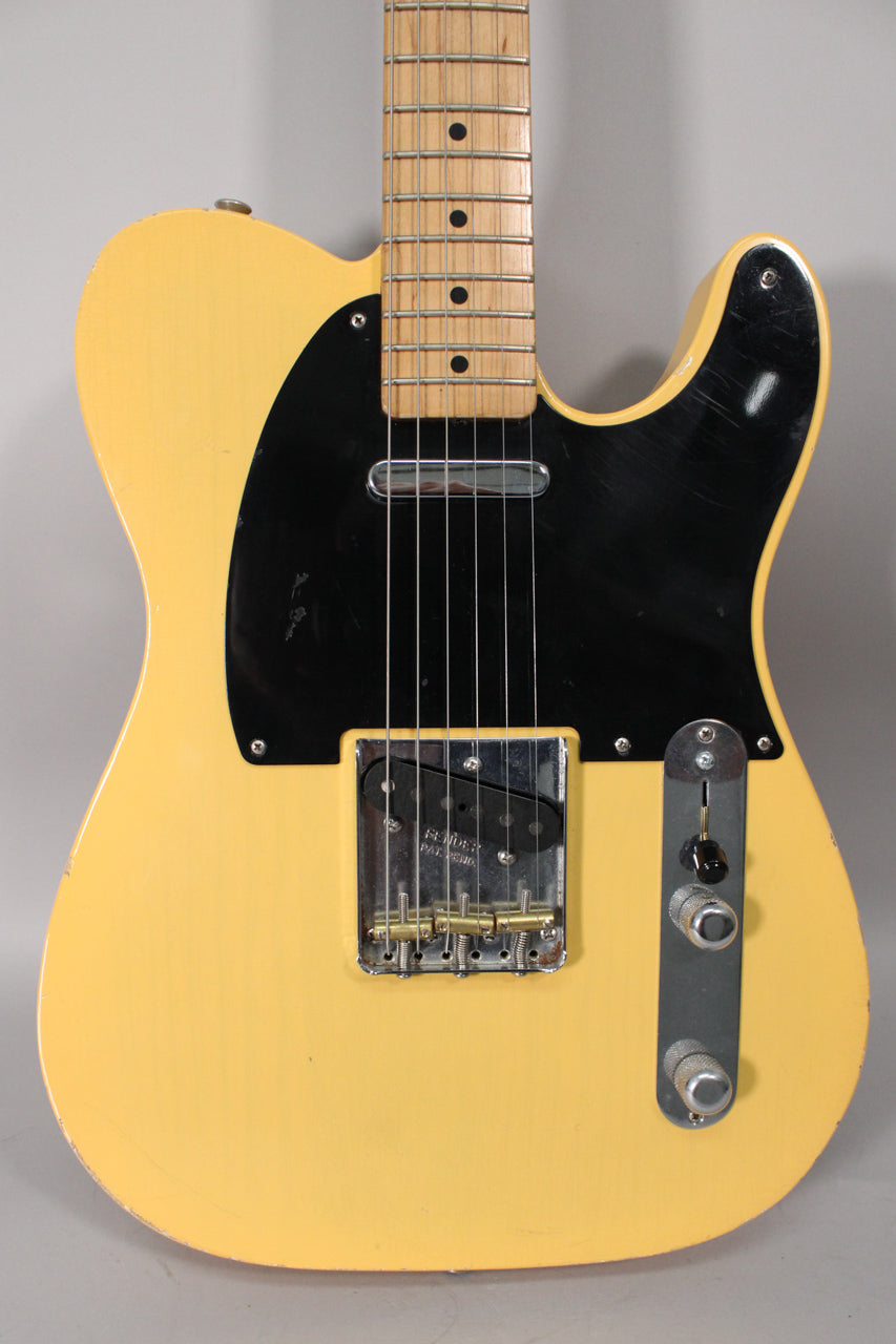 Full-frame view of a blonde Telecaster with a black pickguard, showing a maple neck, chrome bridge, and two knurled chrome knobs.