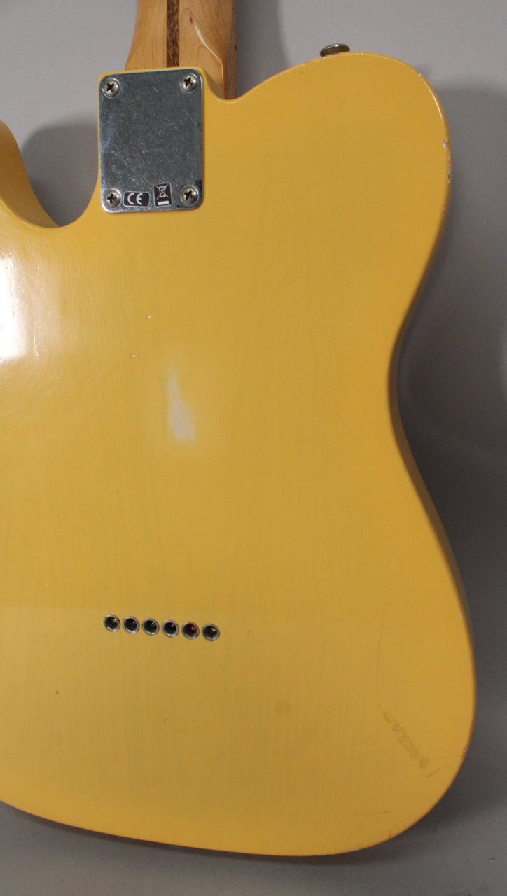The back of a blonde Telecaster body, showing the neck plate, six string ferrules, and a worn finish with visible scuffs.