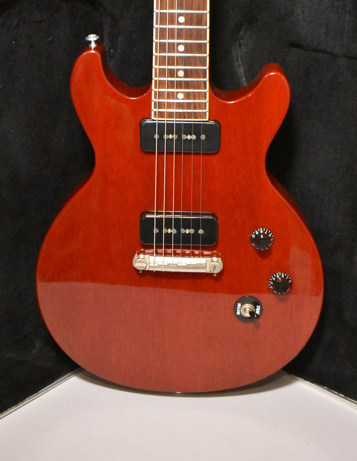 Cherry red double-cutaway electric guitar, framed from the neck to the lower bout, with two P90 pickups and black control knobs.