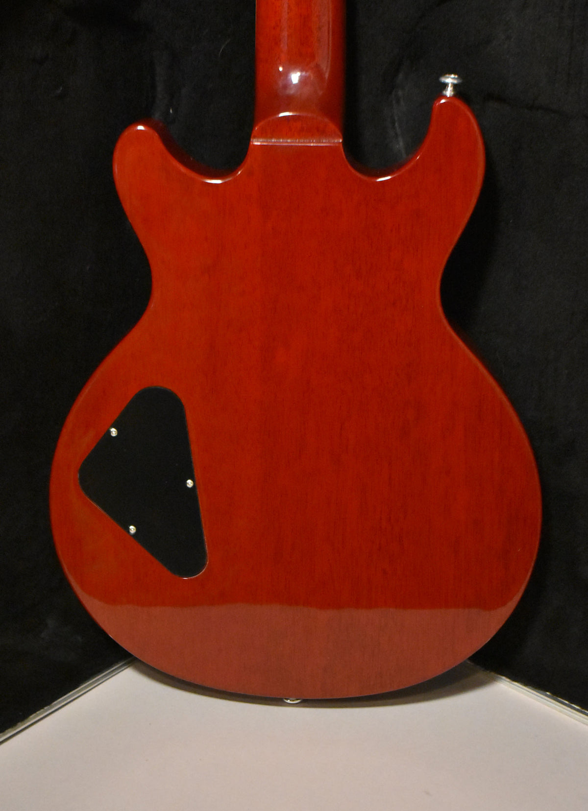 The back of a cherry red electric guitar, showing the neck joint, black control cavity cover, and a strap button.