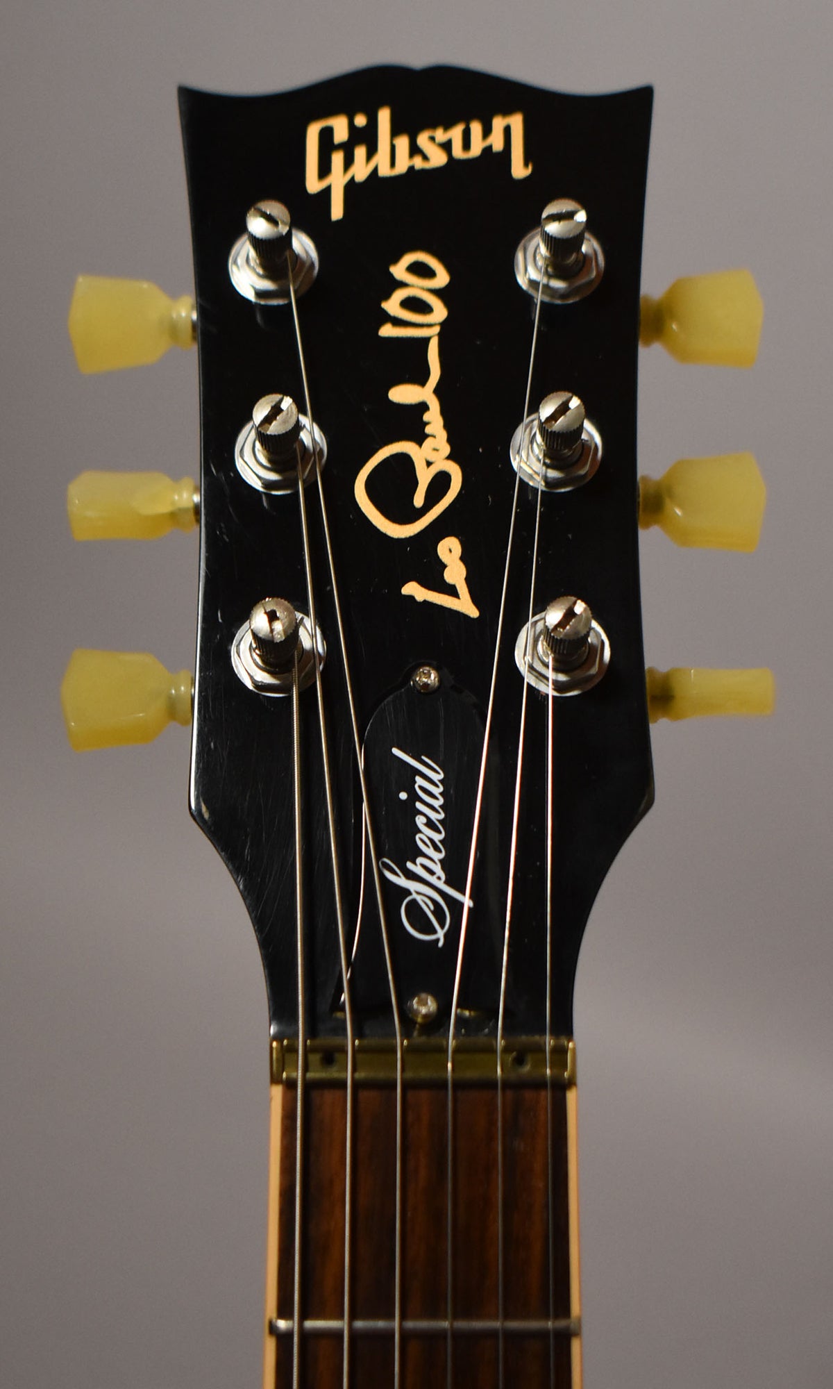Close-up of the guitar's black headstock with light wear, showing six chrome tuners with cream buttons and a dark rosewood fretboard.