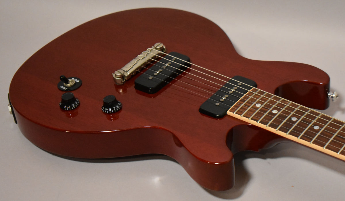 Close-up of a cherry red electric guitar body with two black P90 pickups, a tune-o-matic bridge, and two black control knobs.