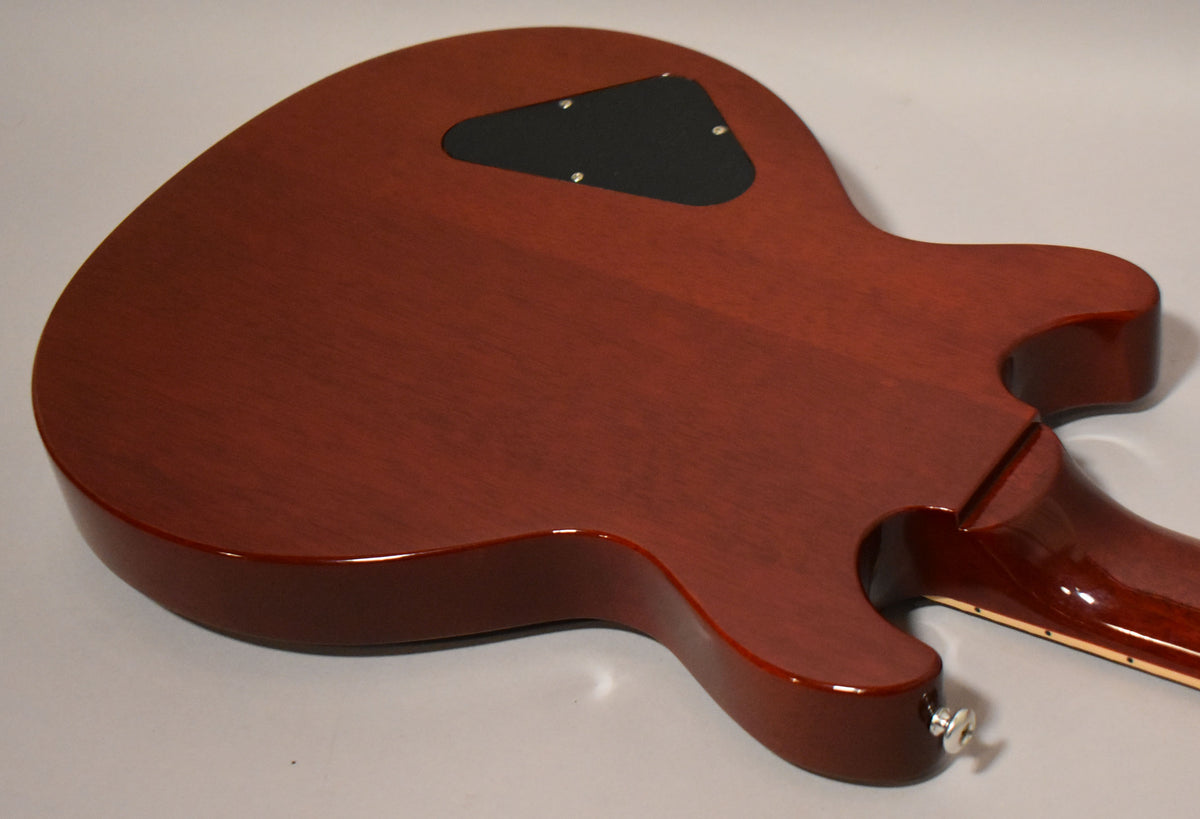 The cherry red guitar's back is angled, showing the glossy body, neck joint, and a black control cavity cover with four screws.