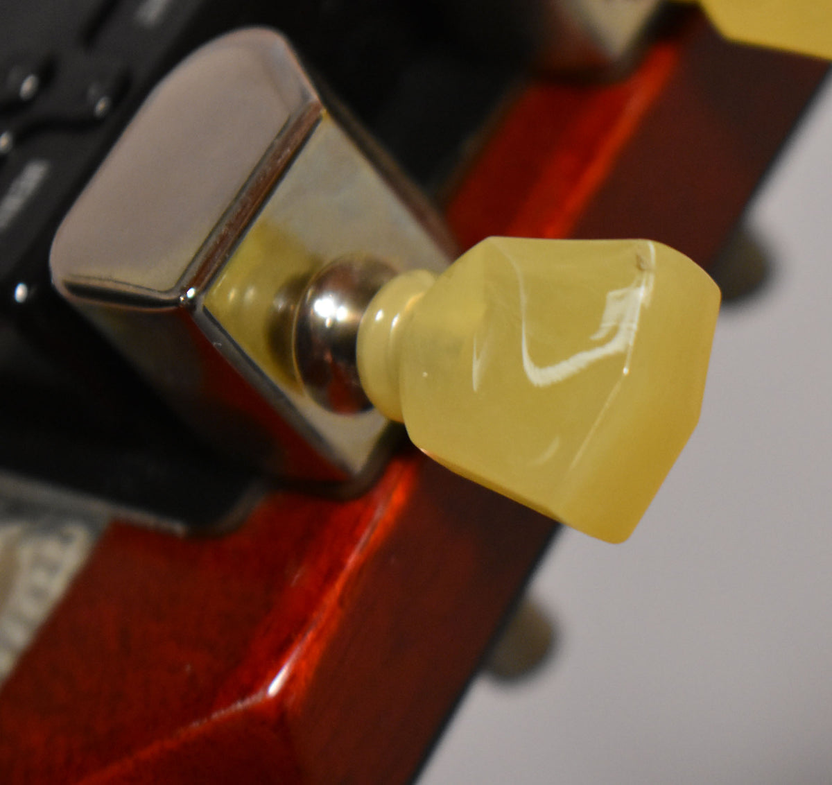 Close-up of a chrome tuning peg with a yellowed trapezoid knob, showing light wear on the cherry red headstock.