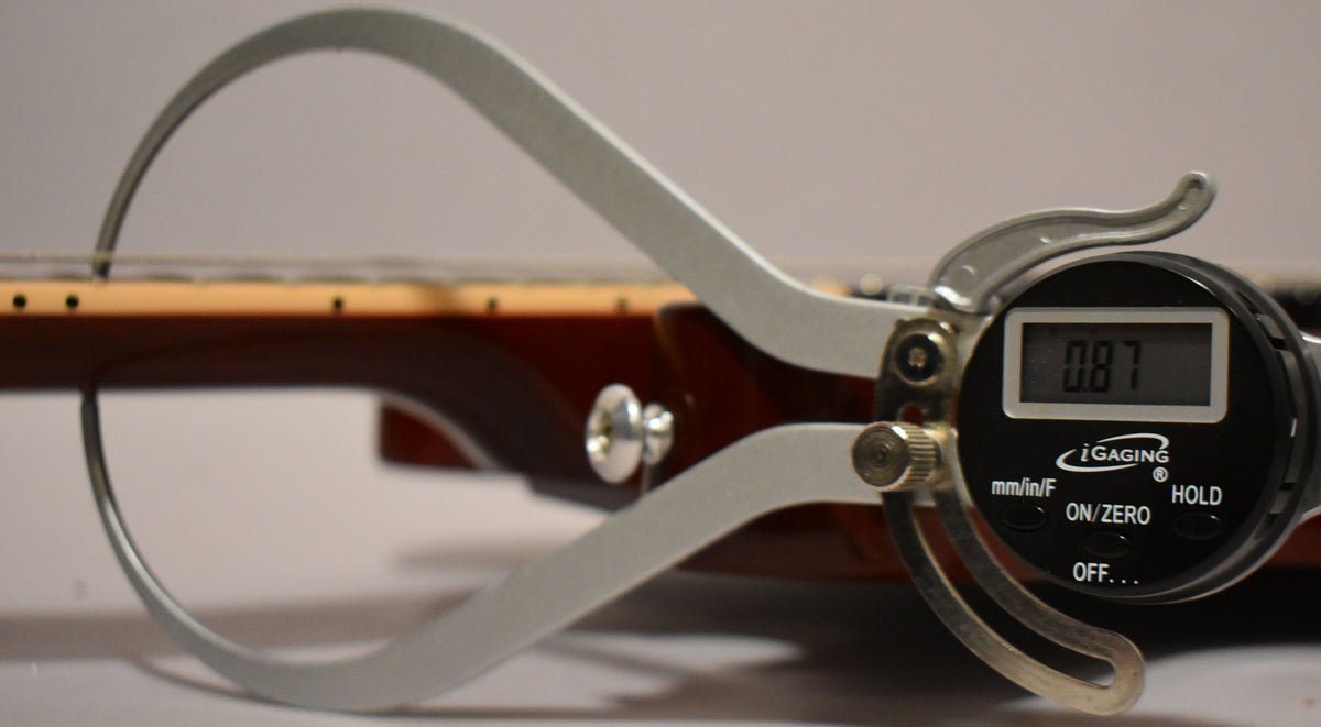 A digital caliper measures the guitar's cherry red body and neck, showing a reading of 0.87.