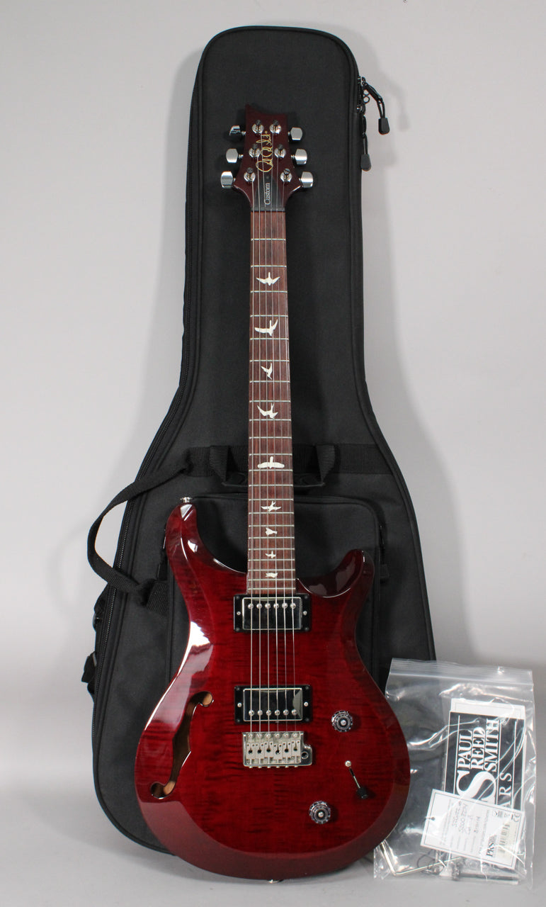 Full view of a trans red semi-hollow electric guitar with a gig bag, showing a flamed maple top, f-hole, and bird inlays.