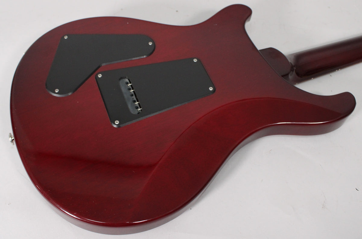 The back of a trans red electric guitar, angled from the lower left, showing two black control cavity covers and a string-through bridge.