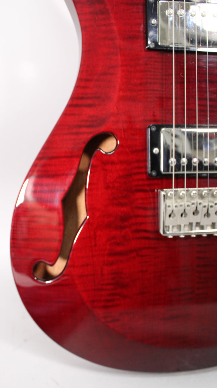 Close-up of the guitar's lower bout, showing the translucent red finish, f-hole, two humbuckers, and chrome tremolo bridge.