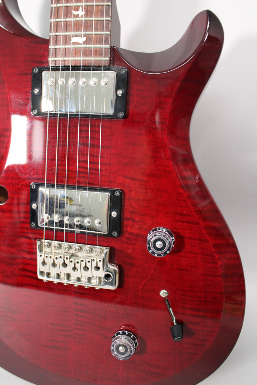 Close-up of the guitar's upper body, showing a translucent red finish, two chrome humbuckers, and two clear numbered control knobs.