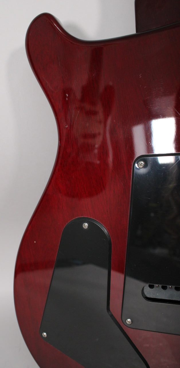 The back of a trans red guitar body, showing two black control cavity covers and many light surface scratches.