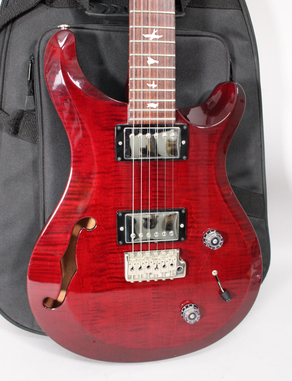 Trans red semi-hollow guitar, angled from above, showing the body's flame maple top, f-hole, two humbuckers, and tremolo bridge.