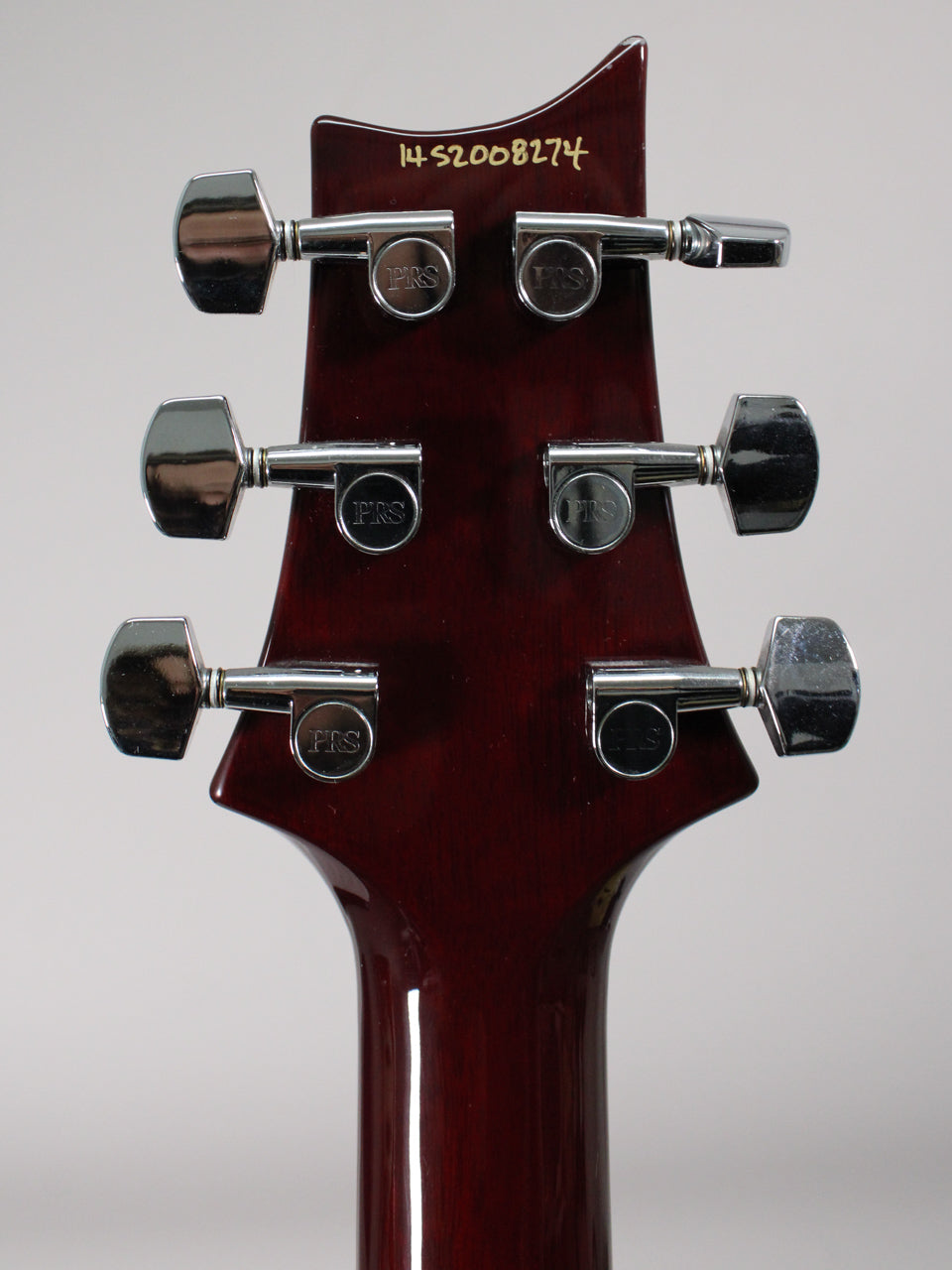 The guitar's dark red headstock, viewed from the back, features six chrome tuners with visible light wear.
