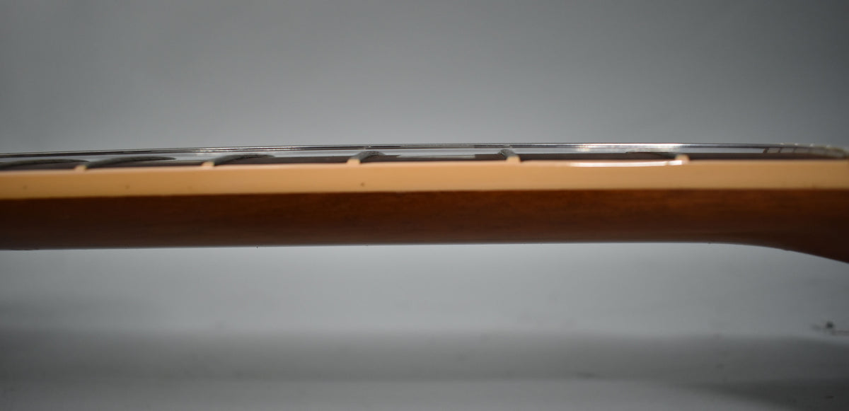 Side view of the guitar neck, showing the light brown wood, frets, and strings against a gray background.