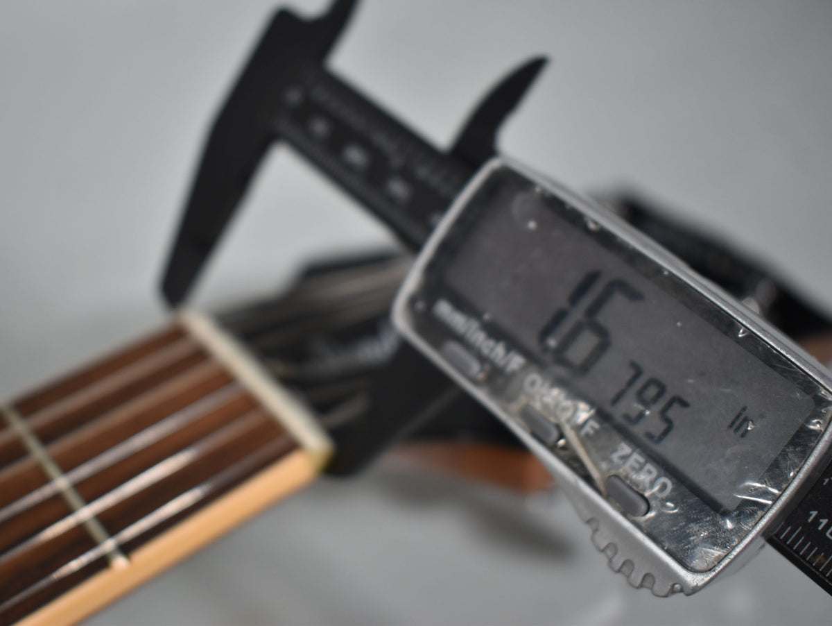 Close-up of the guitar's nut and fretboard, with a digital caliper measuring the nut width at 1.6795 inches.