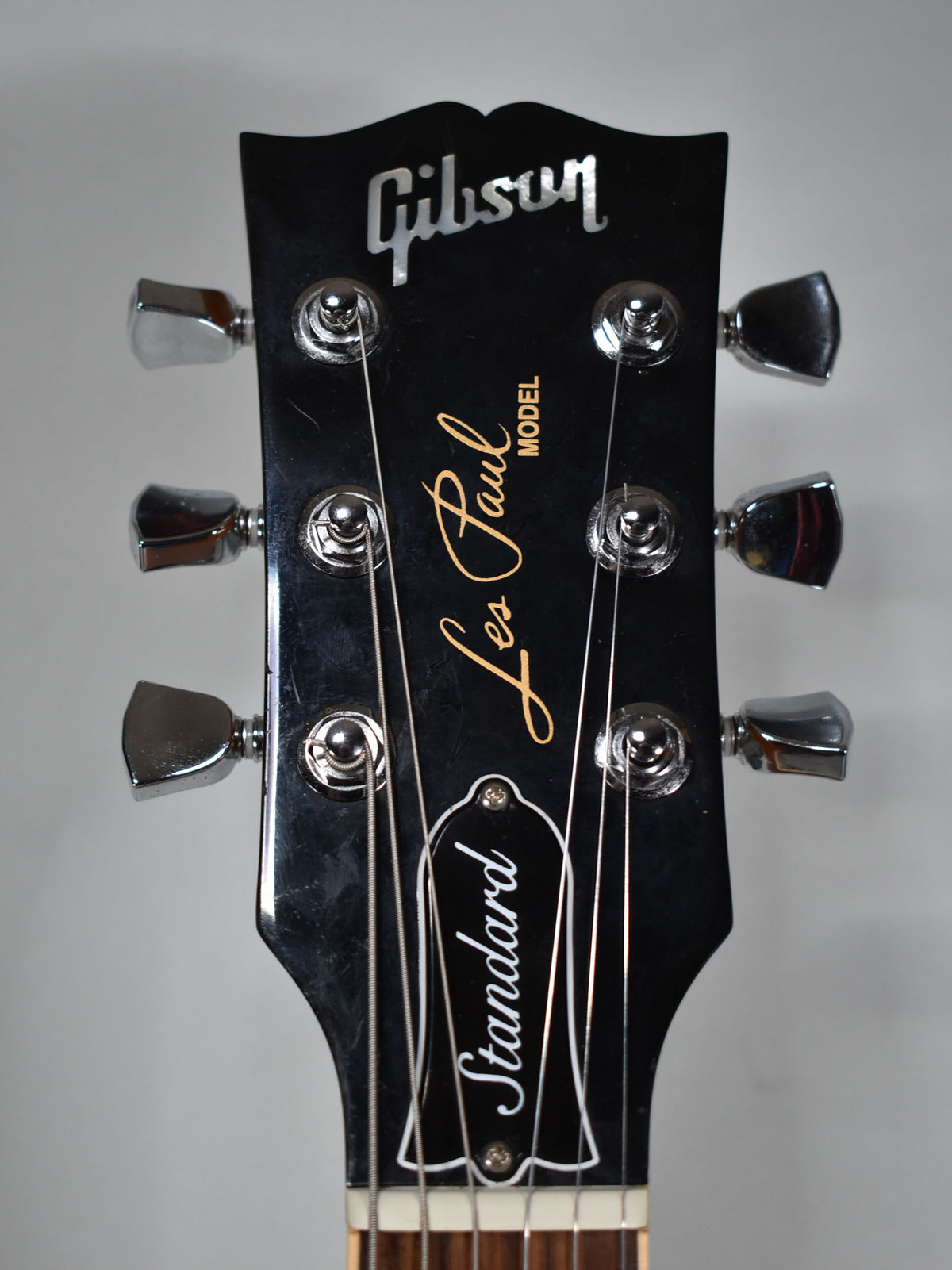 Close-up of the guitar's glossy black headstock, showing six chrome tuners, a white nut, and light surface scratches.
