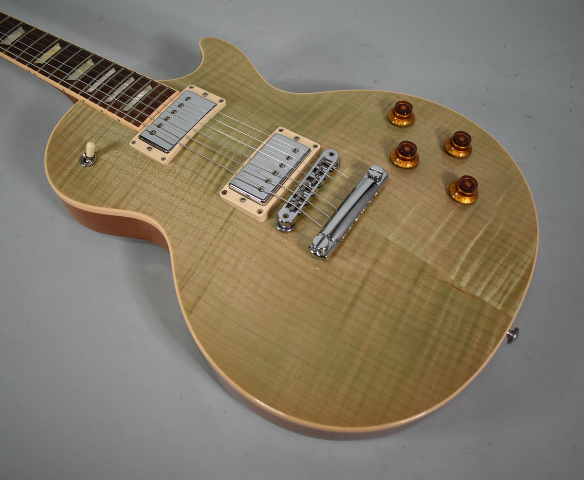 Angled view of a Les Paul's seafoam green flamed maple top, showing chrome hardware, cream pickup rings, and amber control knobs.