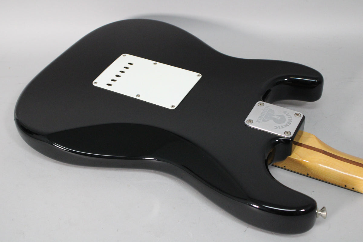 The guitar's glossy black back is angled, revealing a white tremolo cover, a chrome neck plate, and a maple neck.