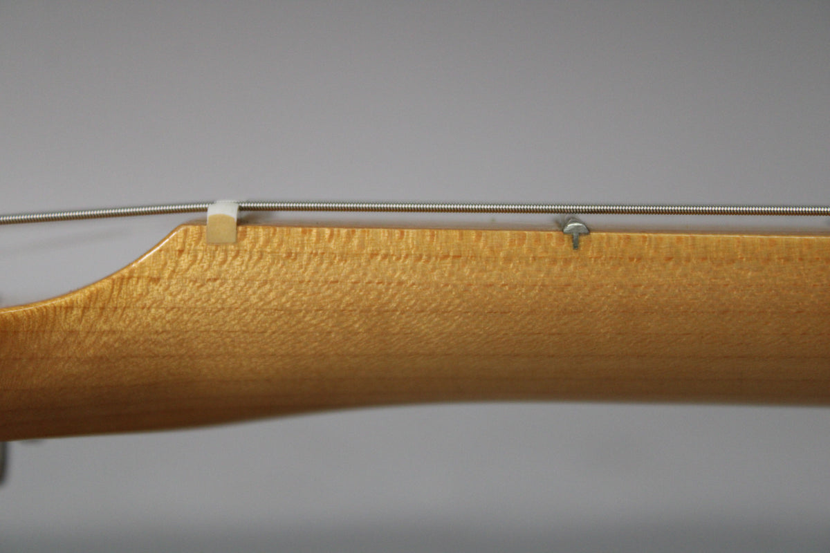 Close-up of the light maple neck and headstock transition, showing a string tree and the nut with strings.