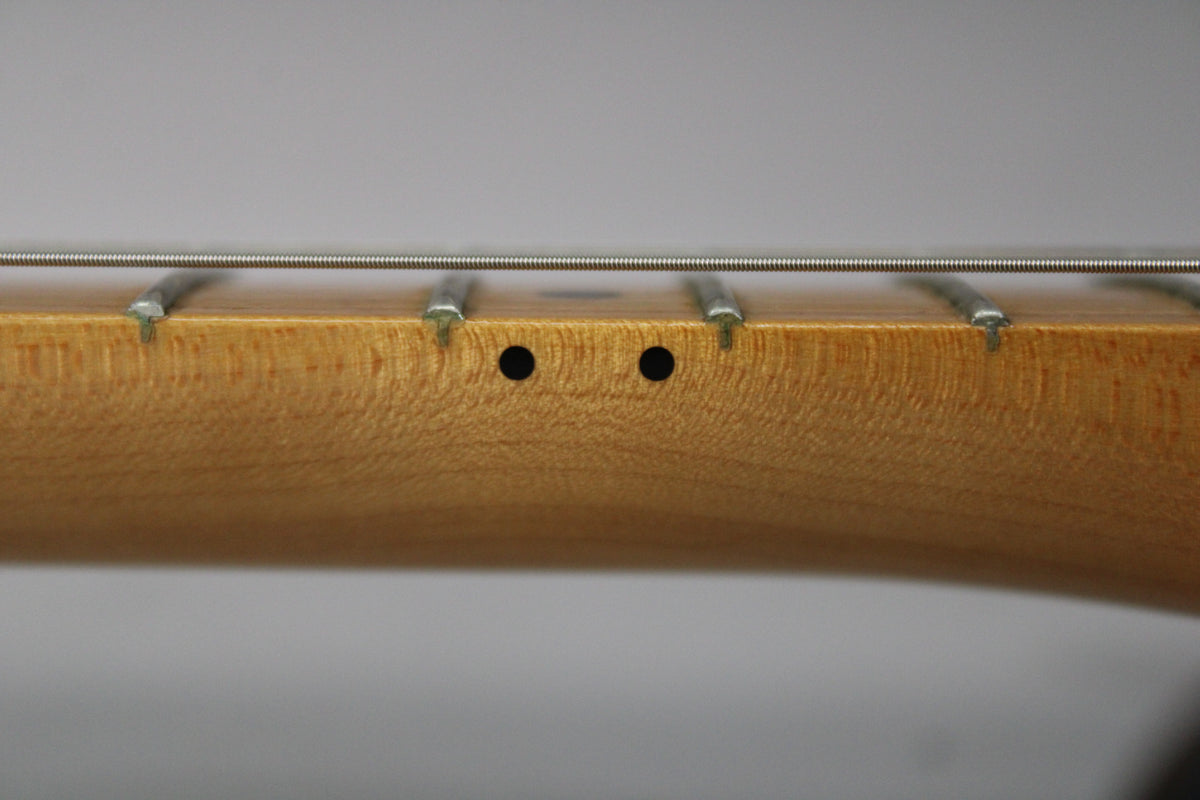 Close-up of the light brown maple neck and fretboard, showing two black dot markers and four frets with strings.