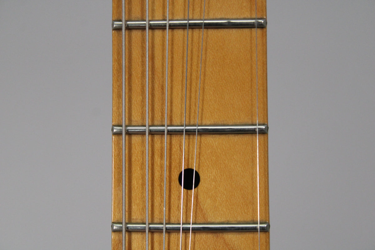 Close-up of the maple fretboard, showing five frets and a single black dot inlay at the 7th fret, with six strings running over them.