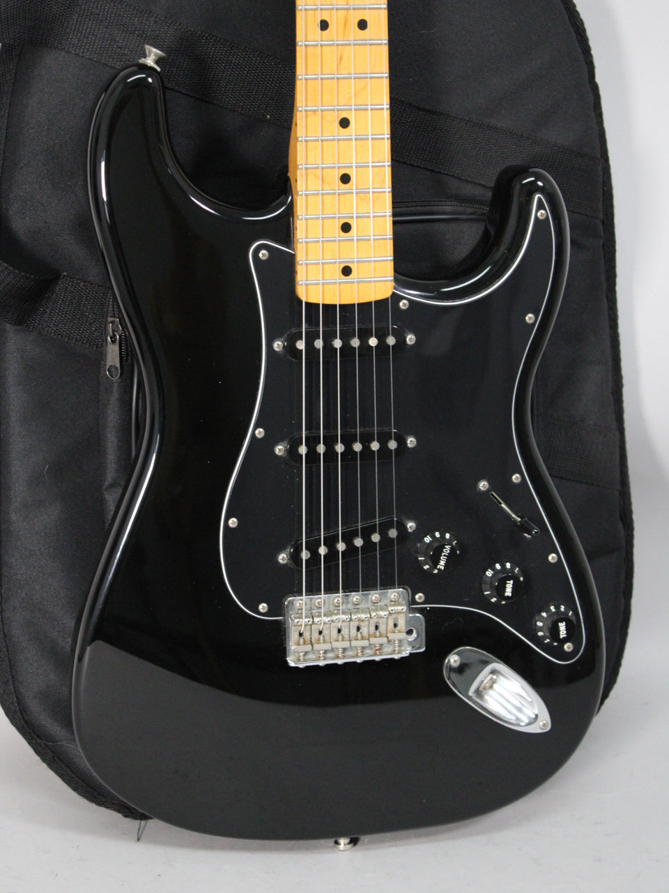 Black electric guitar, body and neck visible, with a maple fretboard, three single-coil pickups, and a chrome tremolo bridge.