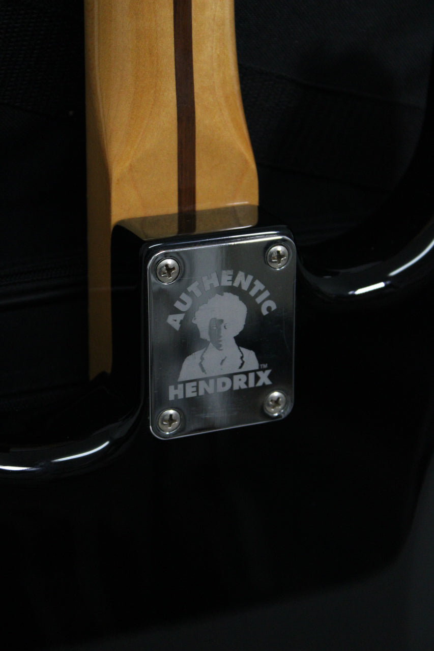 Close-up of the guitar's black body and light wood neck, showing a chrome neck plate with an etched Jimi Hendrix silhouette.