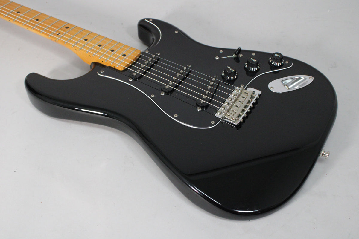 Black electric guitar, angled from the neck to the lower bout, showing a maple fretboard, white pickguard, and chrome hardware.