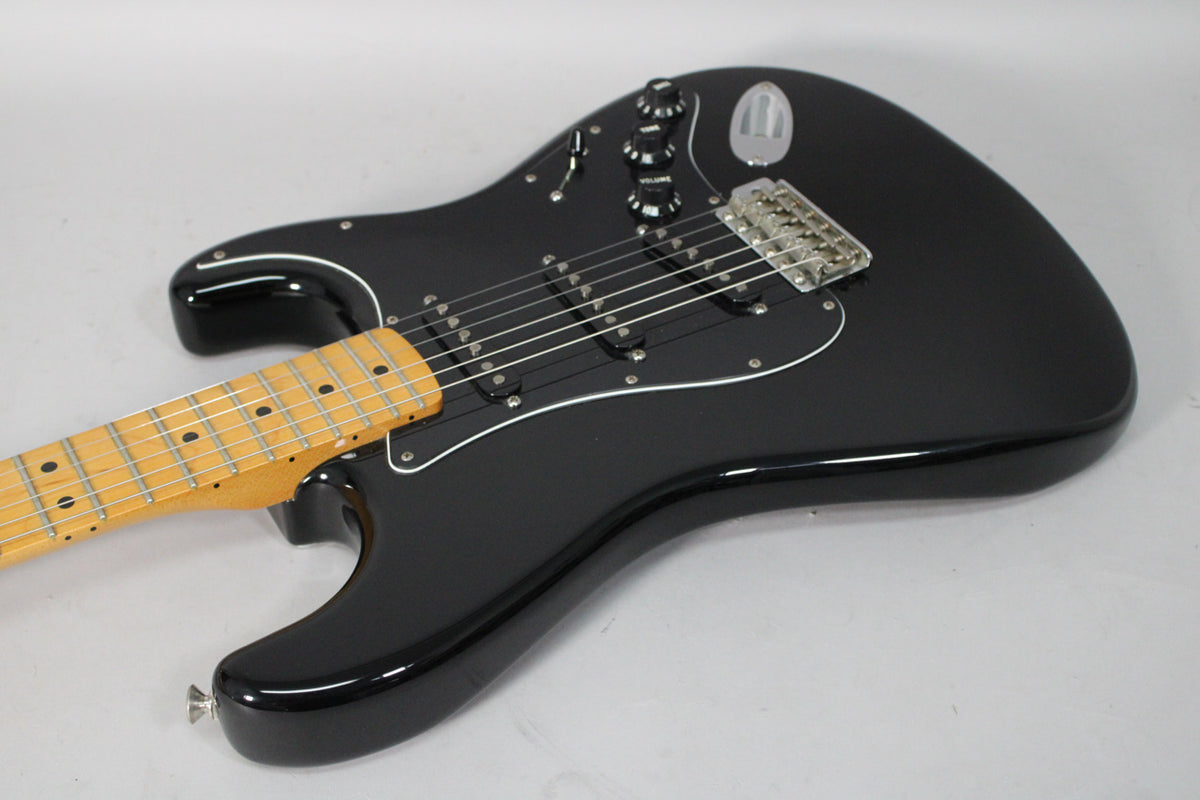 The black Stratocaster's body and neck are angled from the lower left, showing its glossy finish, black pickguard, and maple fretboard.