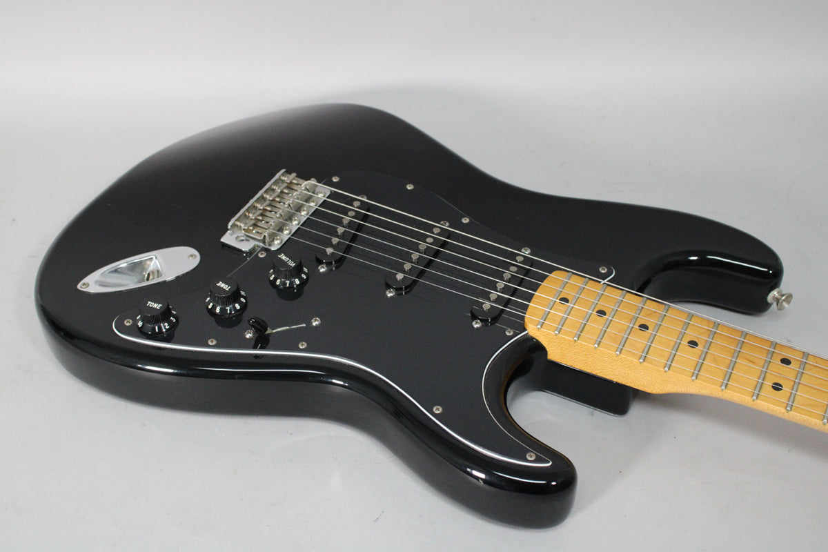 Black Stratocaster with a maple fretboard, black pickguard, three single-coil pickups, and chrome hardware, viewed from the upper bout.