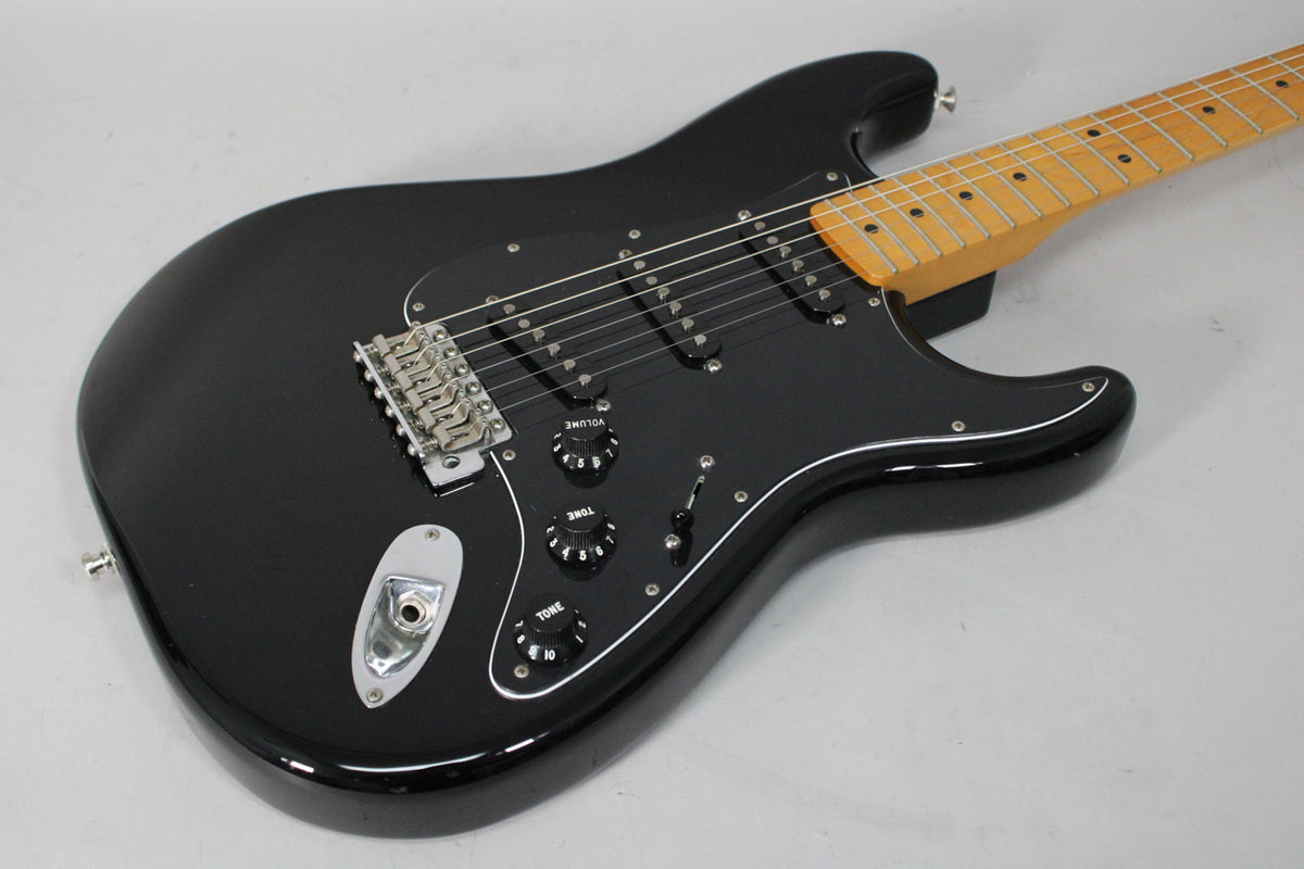 Black Stratocaster, angled from above, showing the glossy body, black pickguard with three single-coil pickups, and maple neck.