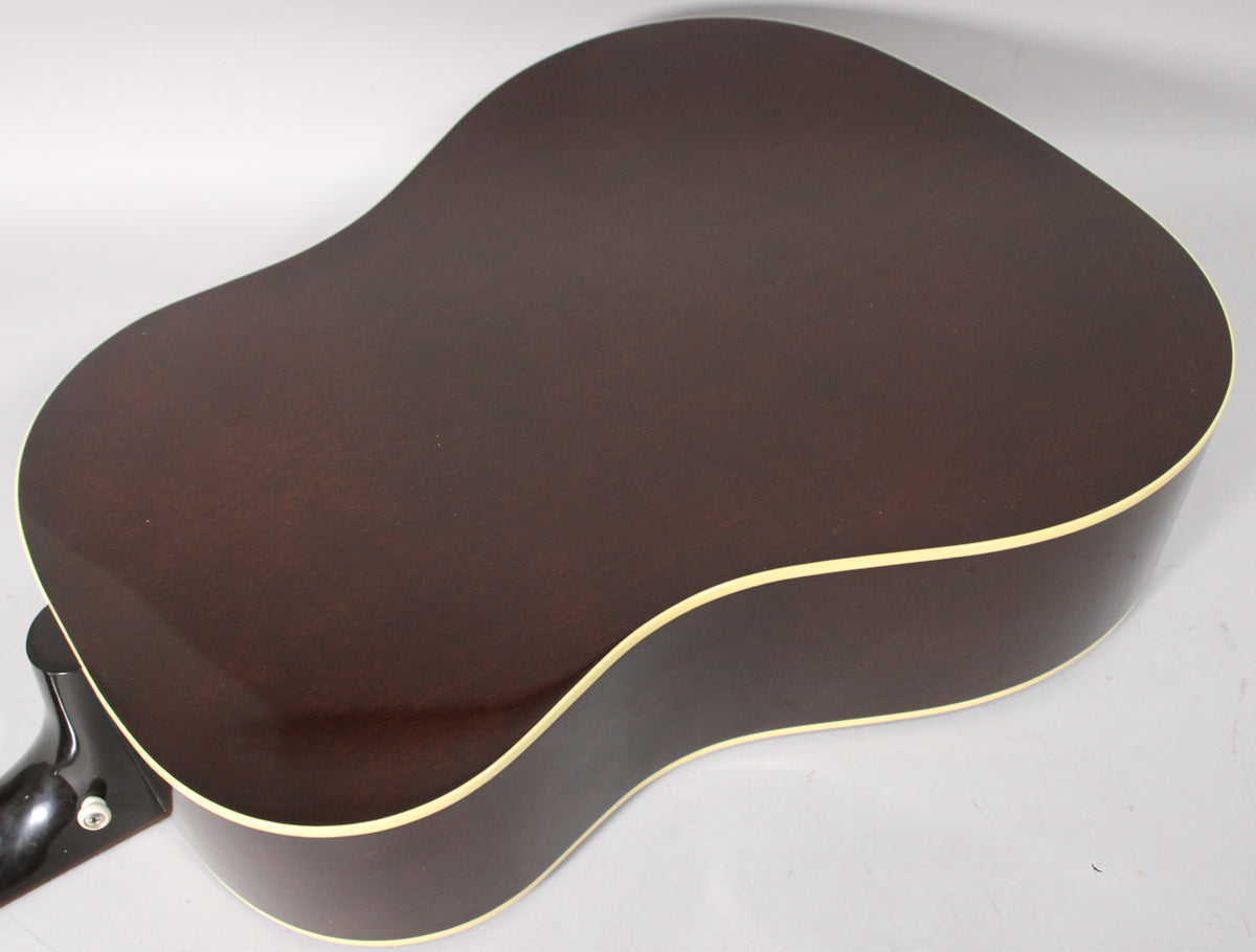 The back of the acoustic guitar, angled from the neck, shows a dark brown finish with light binding and a visible endpin jack.