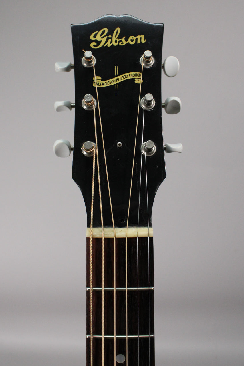 Close-up of the black headstock with "Gibson" in gold script, six white tuning pegs, and the top of the dark fretboard.