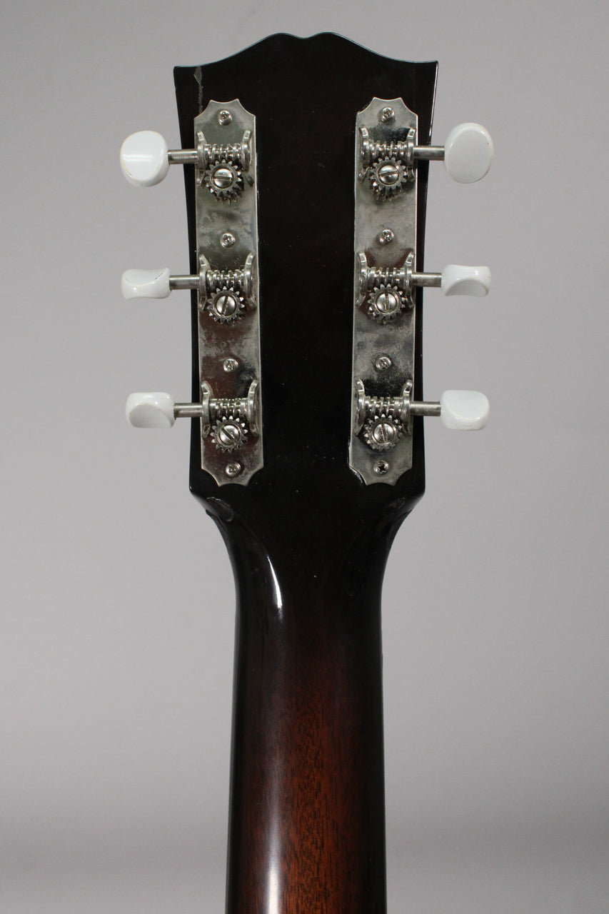 The back of the guitar's dark brown headstock and upper neck, showing six white-buttoned, open-gear tuners with some tarnishing.