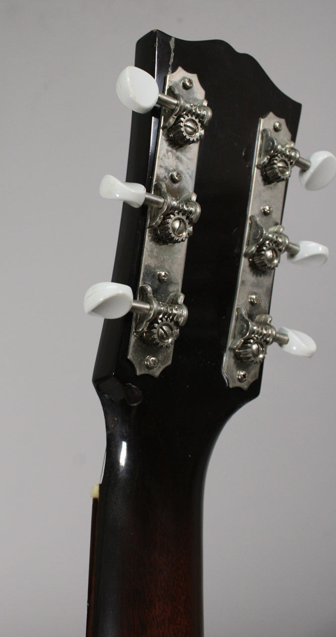 Angled view of the guitar's dark brown headstock and neck, showing six white tuning pegs and two rows of three silver tuners.
