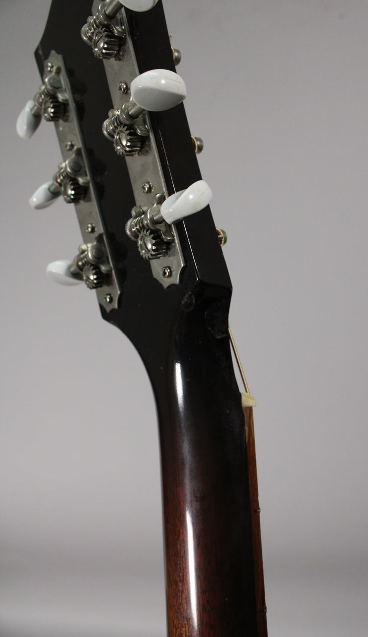Close-up of the guitar's headstock and upper neck, showing six white tuning pegs, a dark glossy finish, and a small chip near the nut.