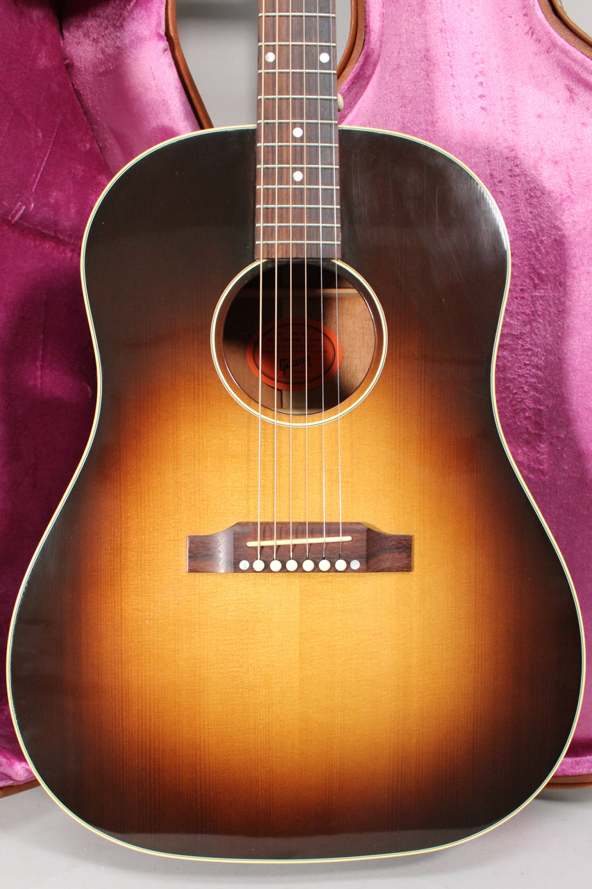 The acoustic guitar's sunburst body, fretboard, and bridge are framed against a purple velvet case, showing light surface scratches.