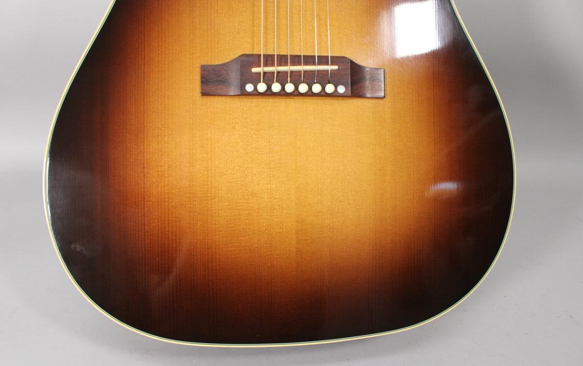 Close-up of the guitar's lower body, showing the dark brown to amber sunburst finish, rosewood bridge, and six white bridge pins.
