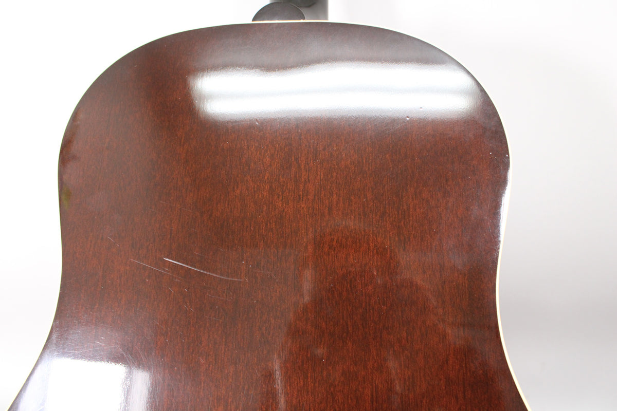 The back of the dark brown acoustic guitar body is shown, with several light scratches and a few small dings visible on the glossy finish.