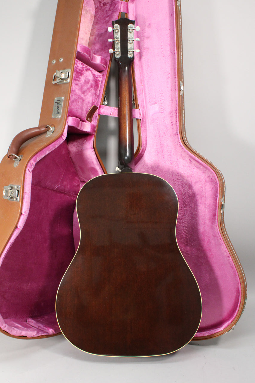 The guitar's dark brown back and neck are visible, with the headstock and tuners resting in a pink-lined brown hard case.