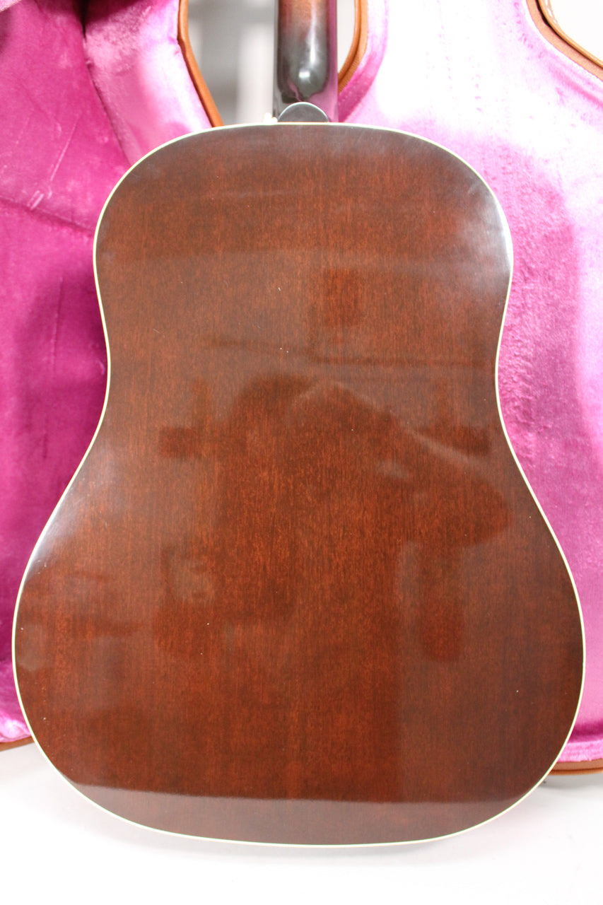 The guitar's dark sunburst back, framed by white binding, shows light surface wear and reflections, with a pink case behind.